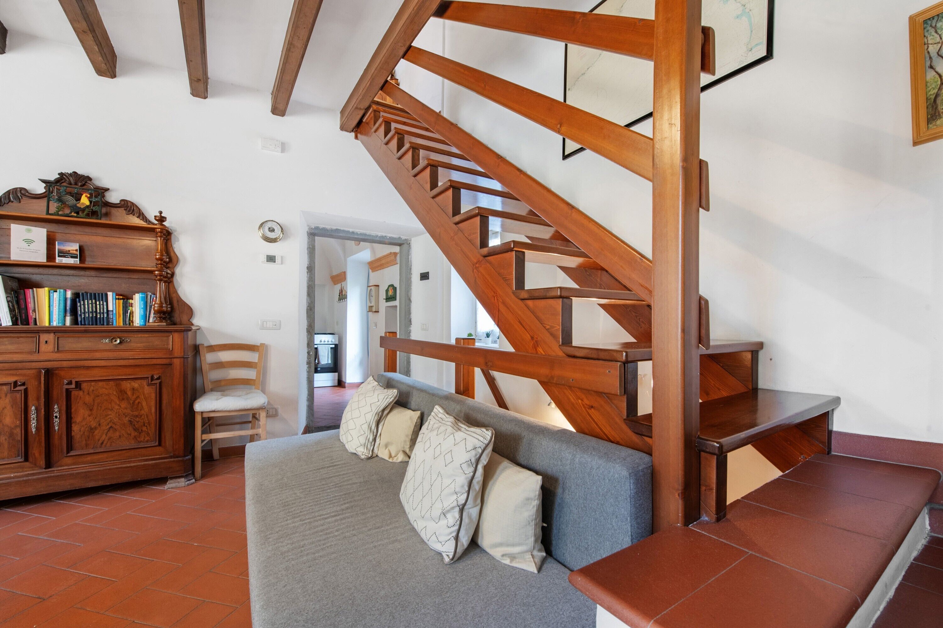 Eine Treppe mit Holzwangen, ein graues Sofa mit Kissen, ein Holzschrank mit Büchern und ein Sessel.
