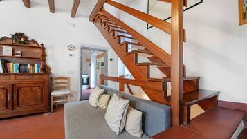 Eine Treppe mit Holzwangen, ein graues Sofa mit Kissen, ein Holzschrank mit Büchern und ein Sessel.