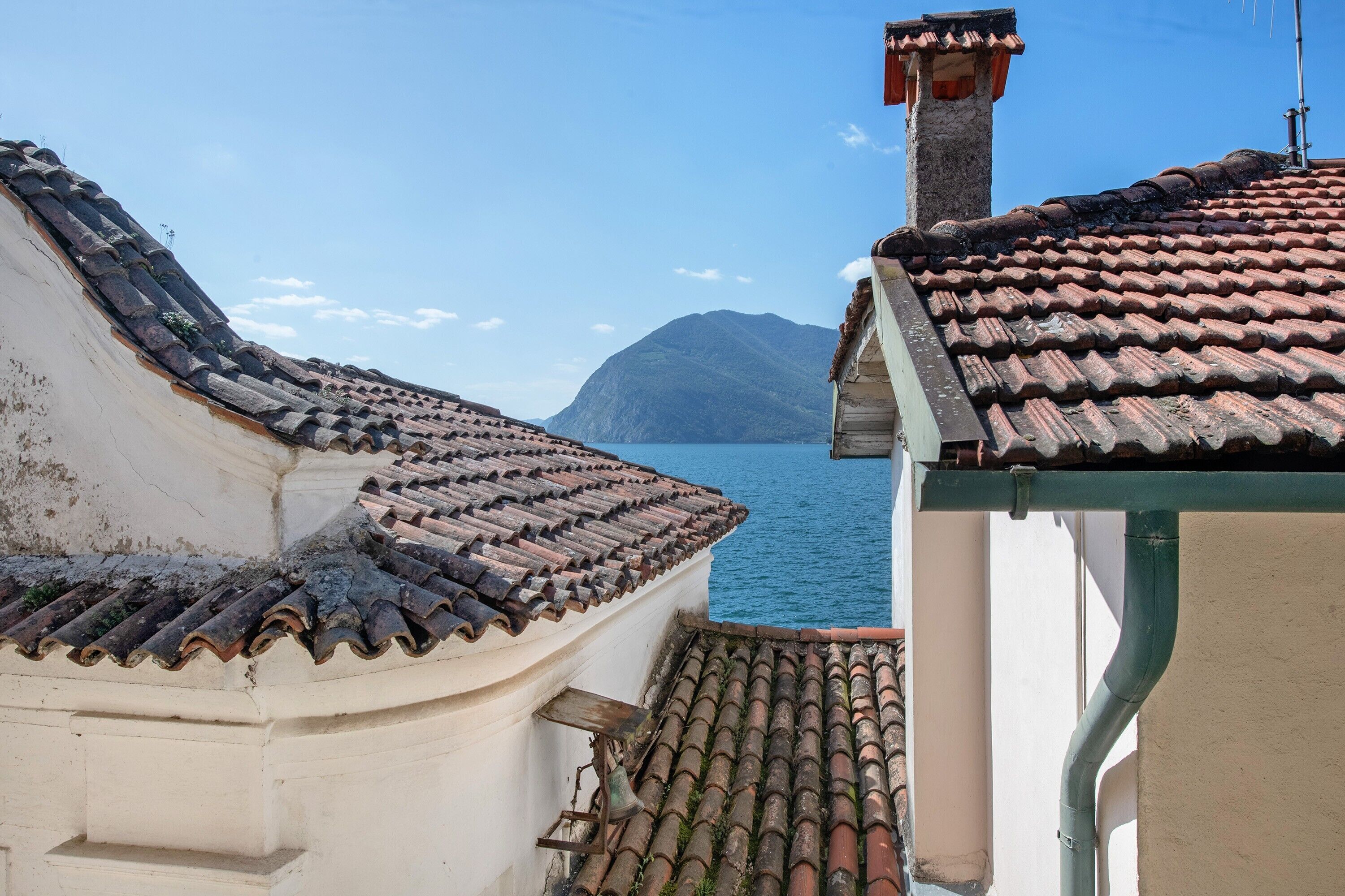 A coastal building with a tiled roof, a chimney, and a view of the sea and a mountain.