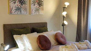 Una cama bien hecha con varias almohadas, una lámpara de noche y una lámpara de pared.