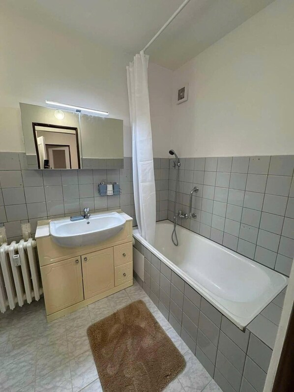 A bathroom with a sink, mirror, shower, and a brown rug. - Apart for Rent Near Center (Prague)
