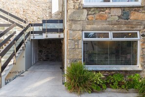 A stone building with a staircase leading to a covered entrance, a window with blinds, and a small garden area with plants. - The Old Salthouse, St Ives – Sleeps 2, On-Site Parking (St Ives)