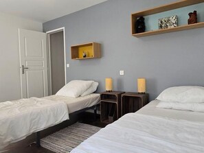 Un dormitorio con dos camas, una puerta, un estante con adornos y dos lámparas de noche.