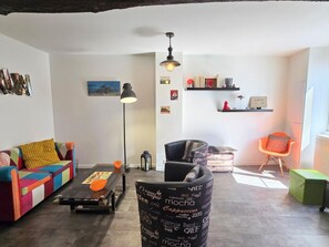 Una sala de estar con un sofá colorido, un sillón negro, una mesa de centro y un reposapiés con forma de grano de café.