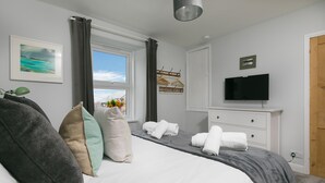A neatly arranged bedroom with a bed, pillows, a TV, and a window with curtains. - Benjamin’s Bolthole, St Ives- Sleeps 4 - Outside Space – Dog-Friendly (St Ives)