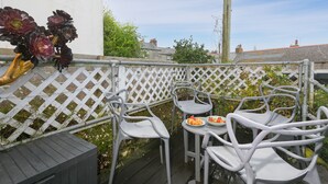 A patio with white metal chairs and a table, a white lattice fence, and a garden with flowers and plants. - Benjamin’s Bolthole, St Ives- Sleeps 4 - Outside Space – Dog-Friendly (St Ives)