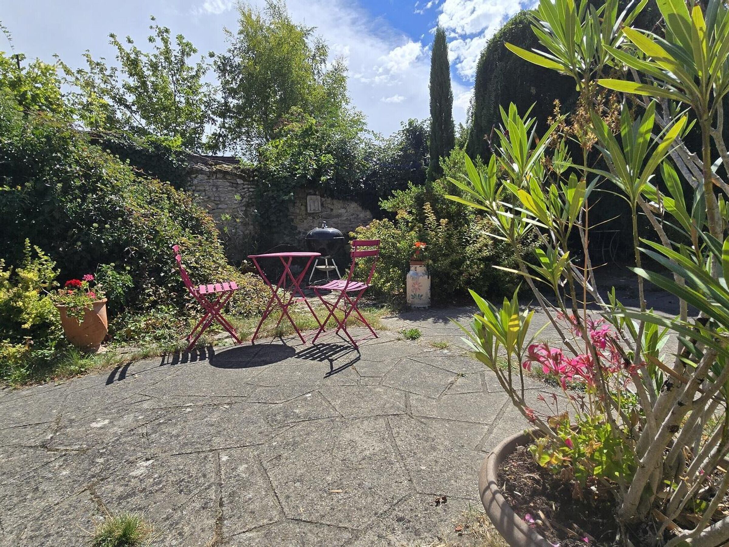 A paved patio with red folding chairs, a stone wall, and various potted plants.