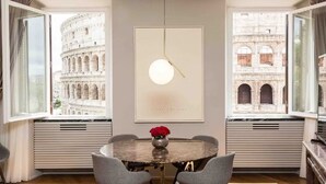 A dining room with a round table, grey chairs, a vase with red flowers, and a pendant light.