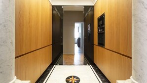 A hallway with wooden walls and a marble floor leading to a room with a black and white patterned rug.