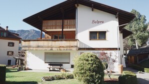 Un edificio a due piani con un balcone, il nome 'Belpra' sulla facciata e una vista chiara sulle montagne sullo sfondo.