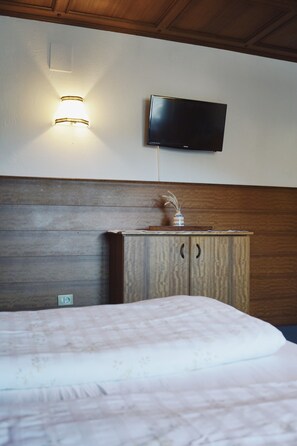 Un dormitorio con cama, cabecera de madera, televisor montado en la pared y lámpara de pared.