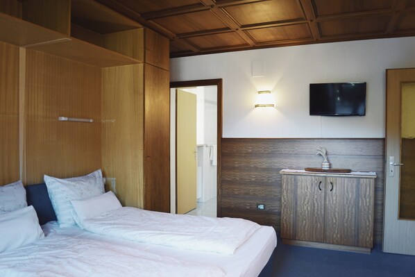 Un dormitorio con cama, armario, tocador y televisor en la pared.