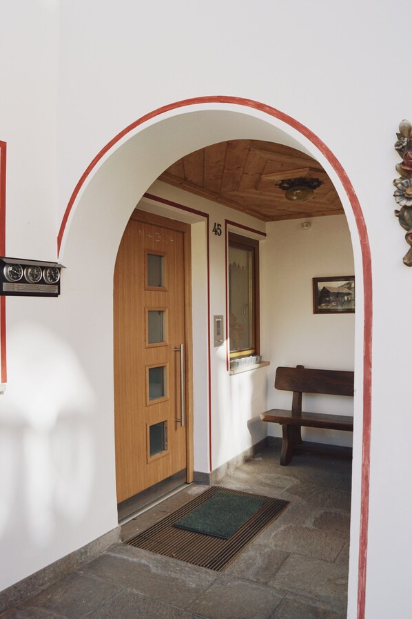 Un couloir avec une porte en bois portant le numéro « 45 », un banc, une horloge fixée au mur et une petite fenêtre.