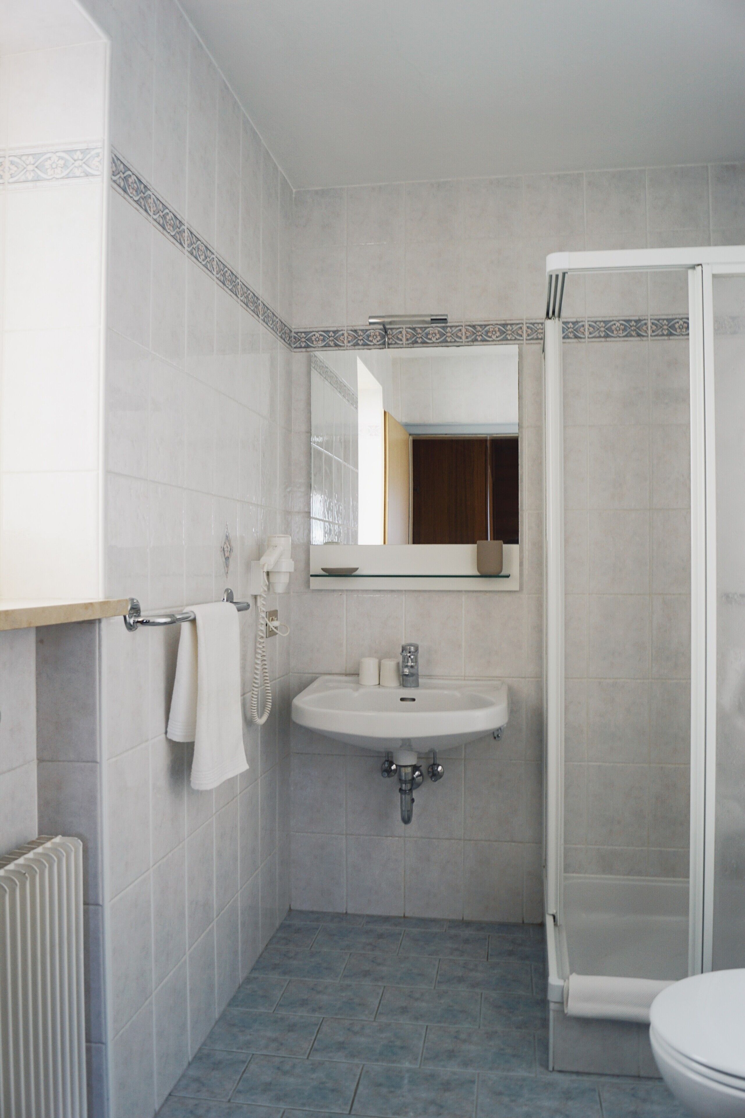 Une salle de bain avec un lavabo blanc, un miroir, un porte-serviettes et une cabine de douche.