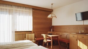 Um quarto com uma cama, um banco de madeira, uma mesa e uma TV fixada na parede.