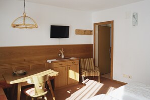 Een kamer met een houten bureau, een stoel, een aan de muur bevestigde televisie, een bed en een deur naar een andere kamer.