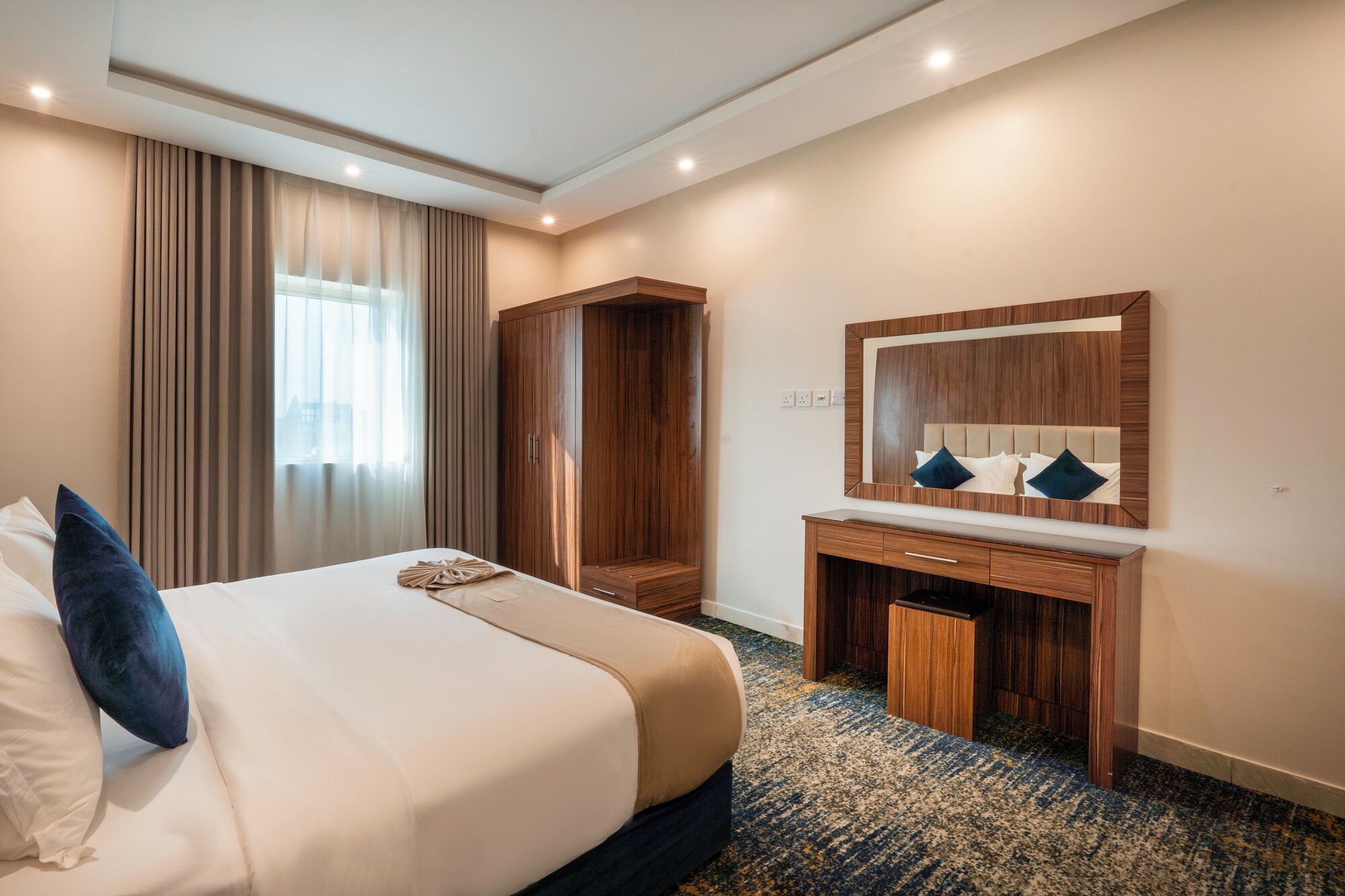 A hotel room with a bed, a wardrobe, a desk, and a mirror.