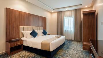 A hotel room with a large bed, wooden headboard, a bedside table, a flat-screen TV, and a carpeted floor.