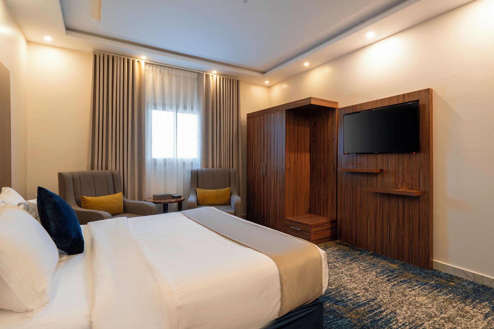 A hotel room with a bed, two armchairs, a television, and a wardrobe.