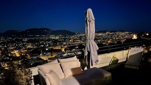 A balcony with a sofa and an umbrella, overlooking a cityscape at night. - NICE 130m2 Terrace with PANORAMIC VIEW, Swimming Pool, Free Parking, A/C, WIFI (Nice)