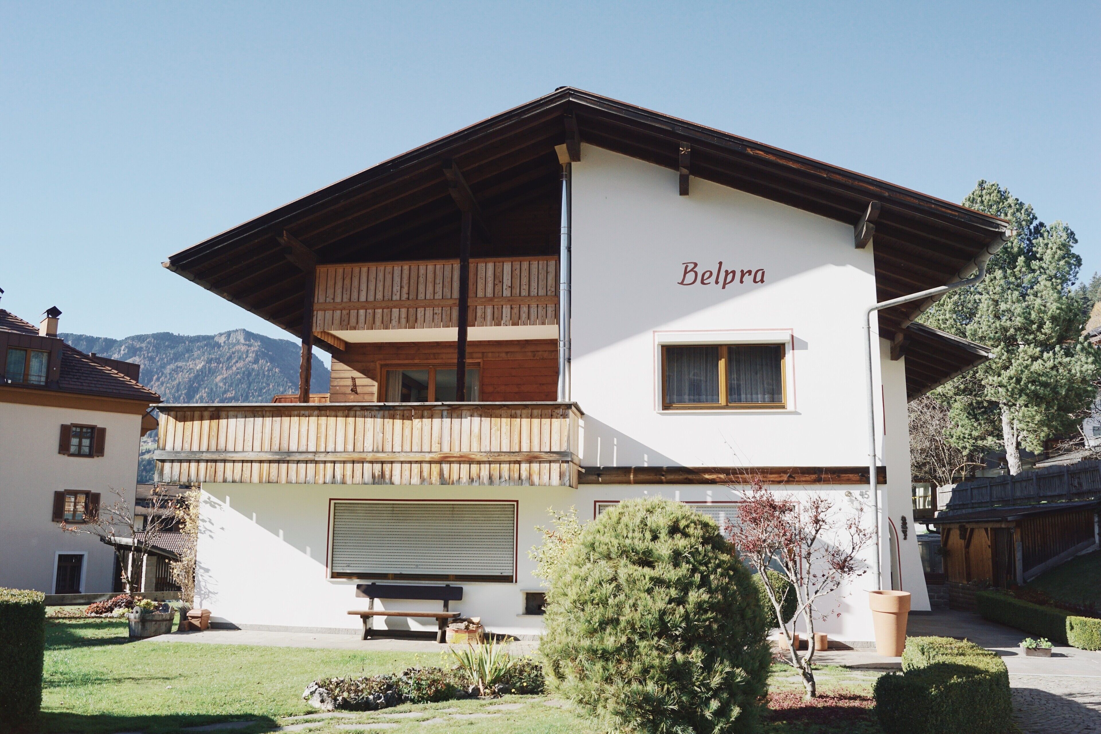 A two-story building with a balcony, a name 'Belpra' on the facade, and a clear view of mountains in the background.