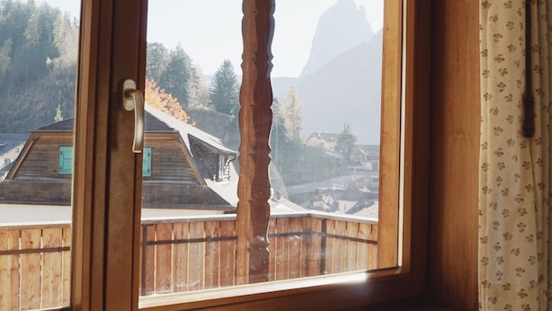A wooden-framed window with a view of a mountain and buildings. - Holiday Apartment '2' with Mountain View, Shared Garden and Wi-Fi (Ortisei)