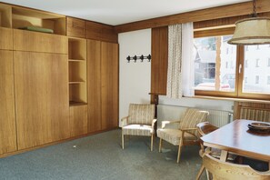 Een kamer met houten meubels, een radiator, een raam met gordijnen en een wandlamp.