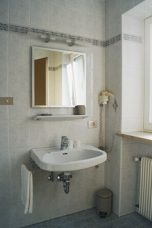 Ein Badezimmer mit Waschbecken, Spiegel, Handtuchhalter und Mülleimer.