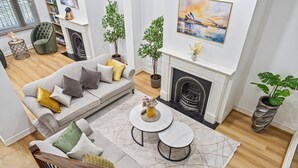 Ein modernes Wohnzimmer mit grauem Sofa, zwei runden Tischen, einem Kamin und Zimmerpflanzen.