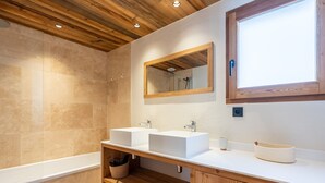 A modern bathroom with two sinks, a wooden vanity, a large mirror, and a bathtub.