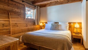 A cozy wooden room with a bed, bedside lamps, and a window.