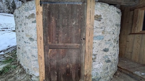 Un edificio rústico de piedra con puerta y escalera de madera, y una ventana.