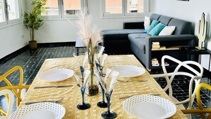 A dining area with a yellow patterned table, white plates, and blue glassware. There is a grey sofa and a small plant in the background. - Spacious apartment in Roses near the beach with parking. (Roses)