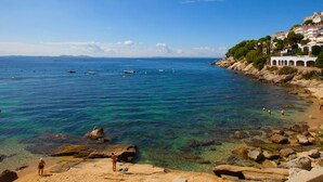A coastal beach with clear waters, rocky shore, and buildings on a hillside. - Spacious apartment in Roses near the beach with parking. (Roses)
