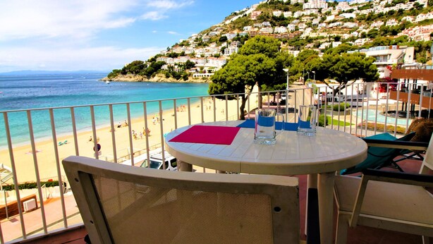 A balcony with a table, chairs, and a view of a beach and hillside buildings. - Spacious apartment in Roses near the beach with parking. (Roses)