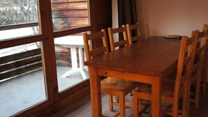 Une table à manger en bois, des chaises, de grandes fenêtres et une vue sur un chalet en bois situé à l’extérieur.