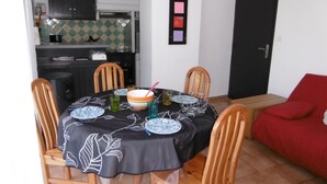 A dining area with a table set for four, surrounded by wooden chairs. A kitchen is visible in the background.