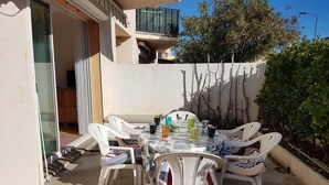 A patio with a table set for four, surrounded by white plastic chairs.