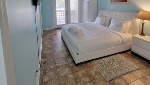 Een slaapkamer met een bed, een plafondventilator, een nachtkastje, een lamp, een deur en een raam.
