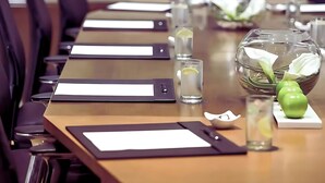 Ein Konferenzraum mit einem langen Tisch, Stühlen, Namensschildern, einer Glasvase mit Blumen und einem Wasserglas.