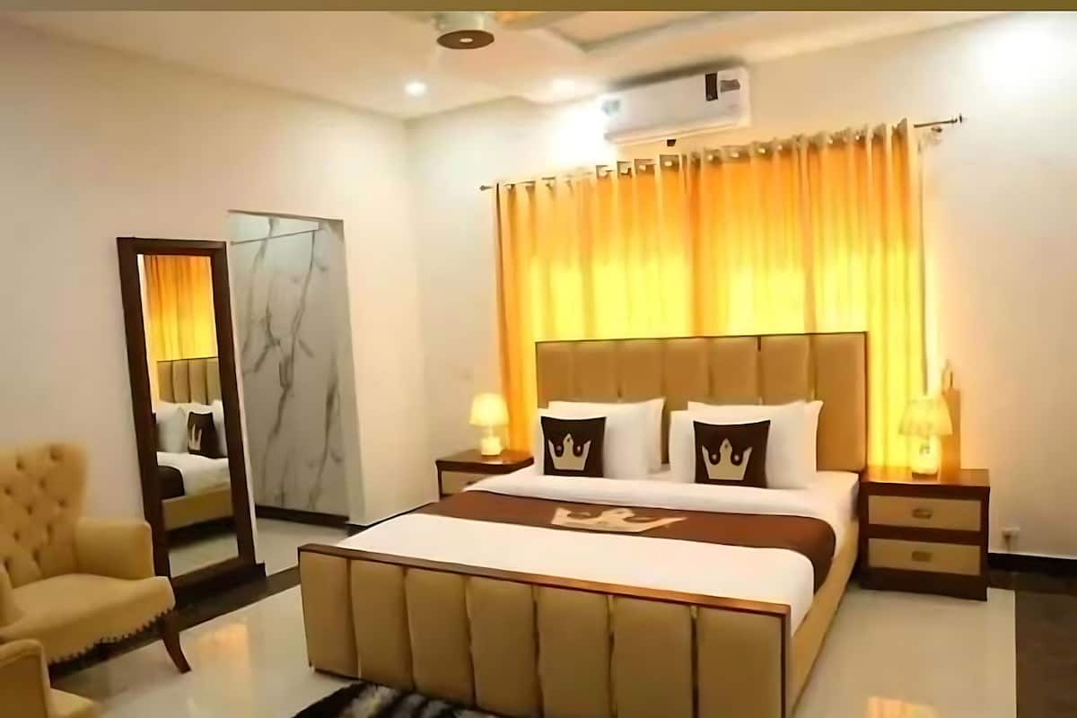 A modern bedroom with a large bed, a mirror, a chair, and an air conditioning unit.
