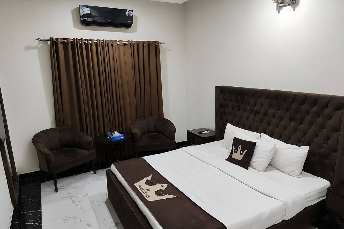 A hotel room with a large bed, two armchairs, a small table, a nightstand, and a wall-mounted air conditioner.