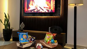 Ein modernes Wohnzimmer mit Flachbildfernseher, einer Couch, einem Couchtisch mit Snacks, einer Lampe und einem Blumentopf.