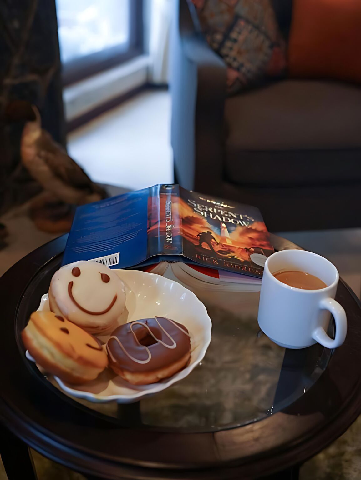 Uma bandeja com donuts e uma xícara de café sobre uma mesa de vidro.