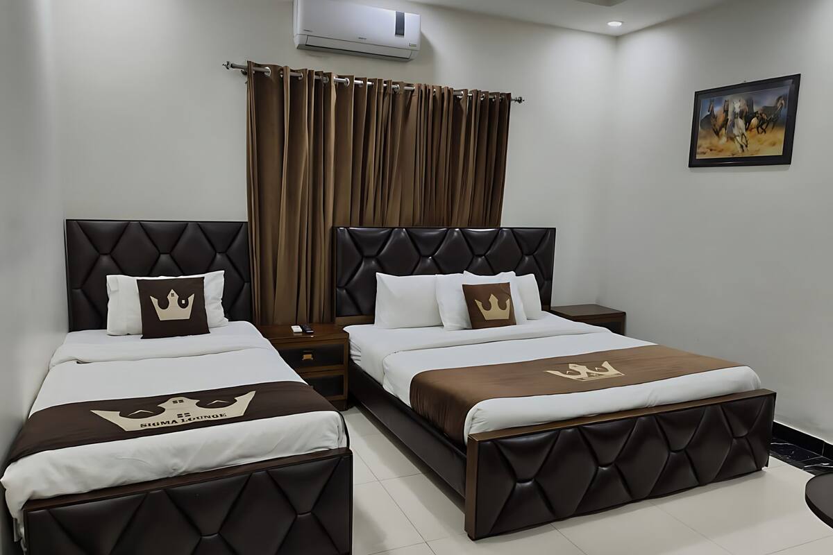 A hotel room with two beds, a nightstand, an air conditioner, and a painting on the wall.