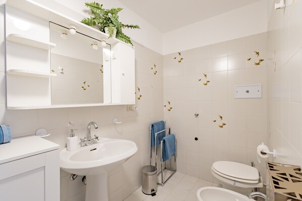 A bathroom with a white sink, mirror, and toilet. There is a plant on the mirror, and the walls have small decorative elements.