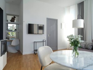 A modern living room with a round marble table, a grey sofa, a white armchair, and a TV mounted on the wall.