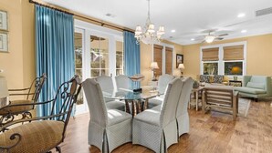 A dining area with a glass table surrounded by chairs, a chandelier, and a view of the outdoors through large windows.