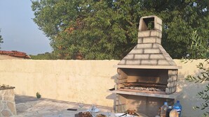 Zona de barbacoa al aire libre con una mesa de piedra dispuesta para comer, un banco de piedra y un horno de pizza.