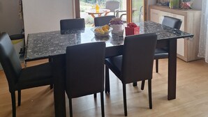 Un comedor con mesa y sillas, vistas al exterior y una kitchenette al fondo.